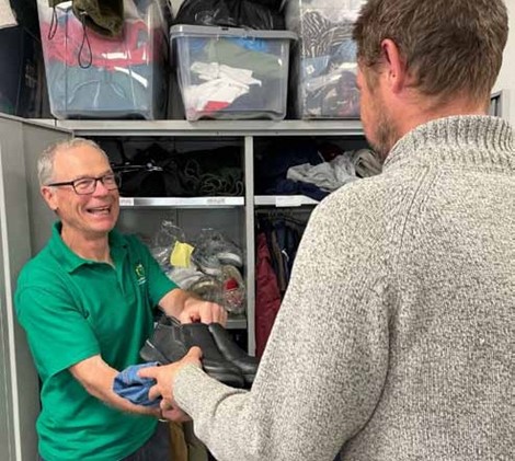 Mick handing a man some shoes and clothing from the store room