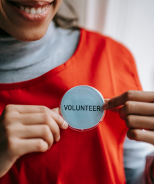 A female in a red tabard with a Volunteer button smiling